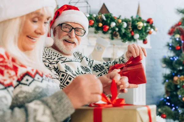 Selective focus of senior woman opening gift box near happy husband — Stock Photo