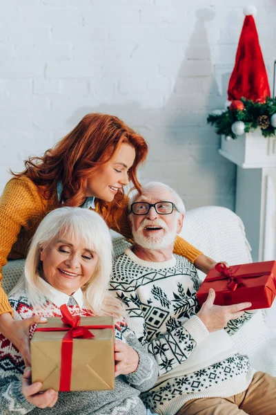 Smiling woman presenting christmas gifts to happy senior parents — Stock Photo