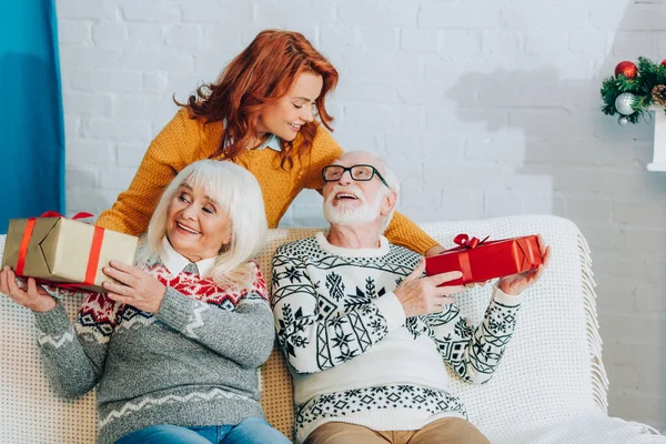 Cheerful daughter presenting christmas gift boxes to happy senior parents — Stock Photo