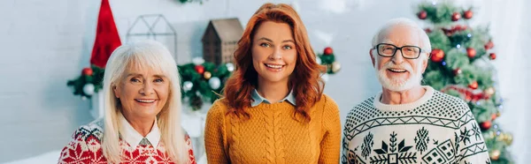 Mujer feliz con los padres mayores mirando a la cámara con decoración de Navidad en el fondo, encabezado del sitio web - foto de stock