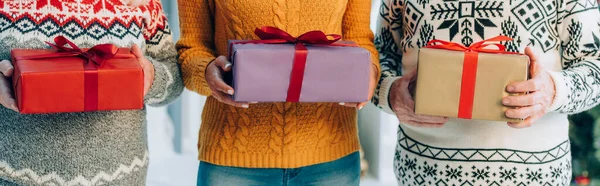 Vista recortada de la mujer y los padres mayores sosteniendo cajas con regalos de Navidad - foto de stock