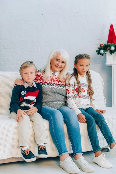 Sorridente donna anziana e nipoti guardando la fotocamera mentre seduti sul divano insieme — Foto stock