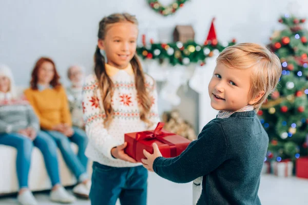 Lächelnder Junge blickt in die Kamera, während er seiner glücklichen Schwester ein Weihnachtsgeschenk überreicht — Stockfoto