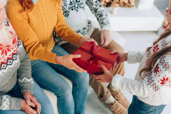 Cropped view of daughter presenting gift box to mother near grandparents — Stock Photo