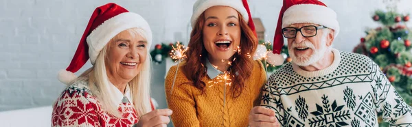Website-Header einer aufgeregten Frau mit älteren Eltern in Weihnachtsmützen mit Wunderkerzen, horizontales Bild — Stockfoto