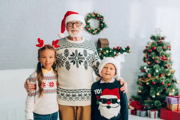 Felice uomo anziano e nipoti in cappelli di Babbo Natale sorridente alla macchina fotografica — Foto stock