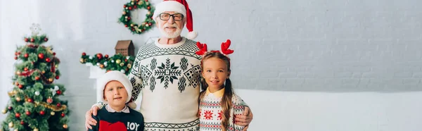 Colpo panoramico di nonno abbracciare nipoti in cappelli di Babbo Natale — Foto stock