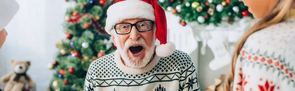 Concept panoramique de vieil homme excité dans le chapeau de père Noël près des petits-enfants — Photo de stock