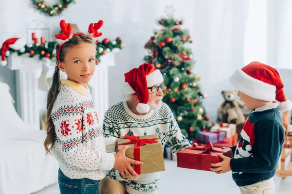 Senior homme dans santa chapeau prendre des cadeaux de petits-enfants sur Noël — Photo de stock