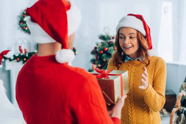 Vista posterior del hombre que presenta el regalo de Navidad a la esposa sorprendida - foto de stock