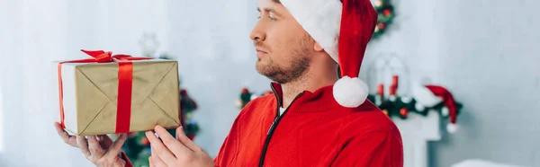 Plan panoramique de l'homme dans le chapeau santa tenant boîte cadeau de Noël — Photo de stock