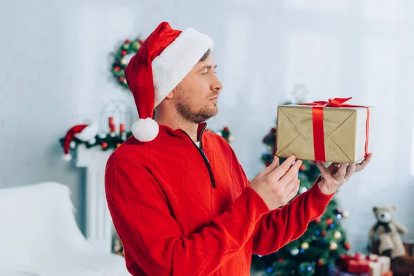 Homem de camisola vermelha e chapéu de santa segurando caixa de presente de Natal — Fotografia de Stock