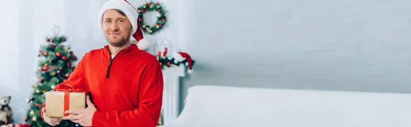 Website header of man in santa hat looking at camera while holding gift box — Stock Photo