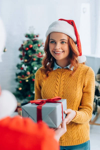 Enfoque selectivo de la mujer feliz en santa sombrero tomando caja de regalo del marido - foto de stock