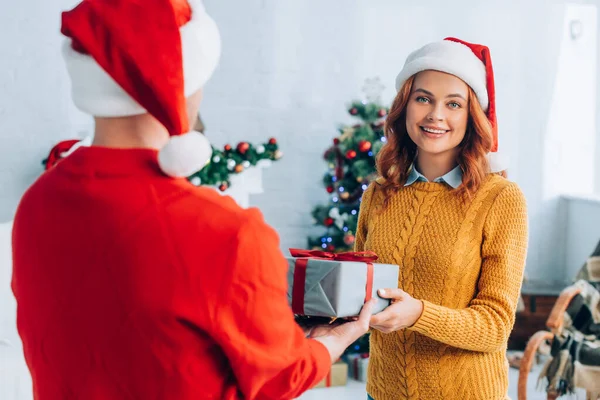 Back view of man in santa hat presenting christmas gift to happy wife — Stock Photo