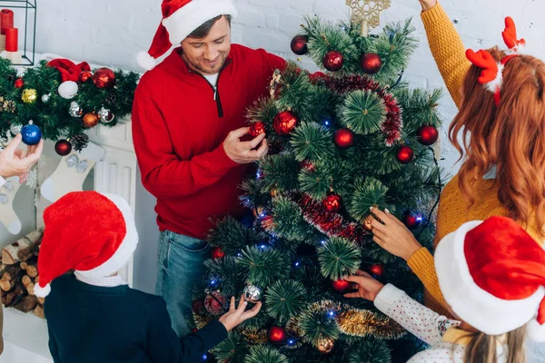 Glückliche Familie in Weihnachtsmützen schmücken Weihnachtsbaum zusammen zu Hause — Stockfoto