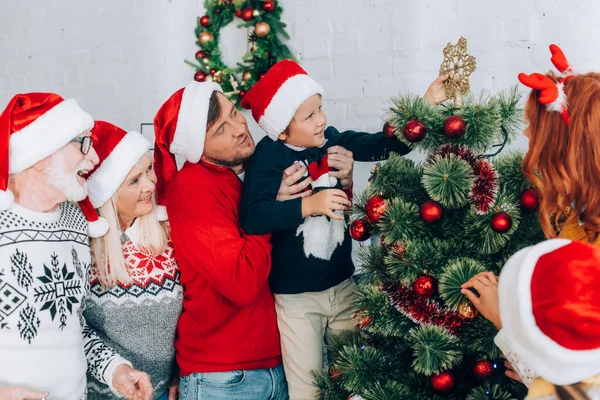 Vater hält Sohn beim Weihnachtsbaumschmücken mit Familie in den Händen — Stockfoto