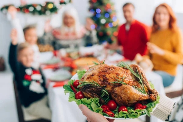 Foco seletivo do homem sênior segurando prato com peru torrado tradicional, tomate cereja e alface durante o jantar de natal com a família — Fotografia de Stock