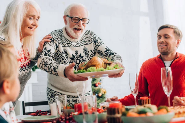 Selective focus of senior man standing near wife, serving turkey on table — Stock Photo