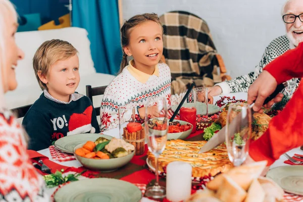 Enfoque selectivo de los niños sentados en la mesa festiva cerca del padre cortando pastel - foto de stock