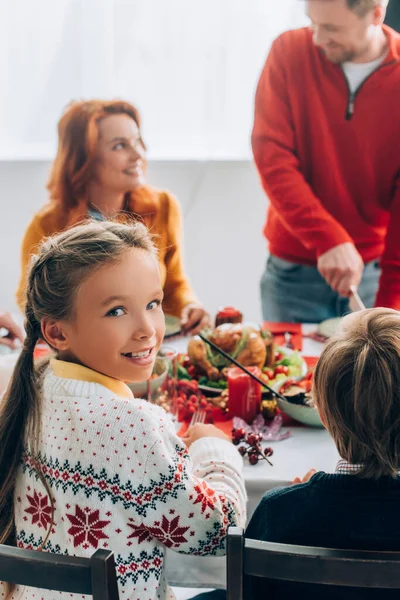 Selective focus of girl looking at camera, sitting at festive table with family — Stock Photo