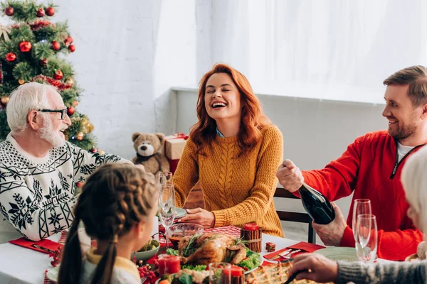 Focus selettivo della donna che ride vicino all'uomo aprendo una bottiglia di champagne a casa — Foto stock