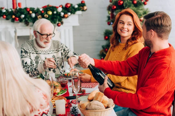 Selective focus of woman looking at man opening champagne bottle near relatives — Stock Photo