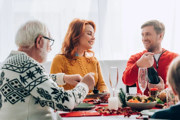 Enfoque selectivo de la esposa hablando con el marido botella de apertura, sentado en la mesa - foto de stock