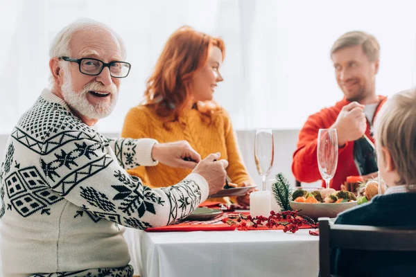 Enfoque selectivo de abuelo sirviendo comida cerca de pareja hablando, en casa - foto de stock