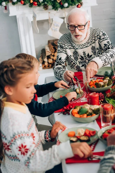 Focus selettivo dell'uomo anziano seduto vicino ai bambini, seduto vicino al camino — Foto stock