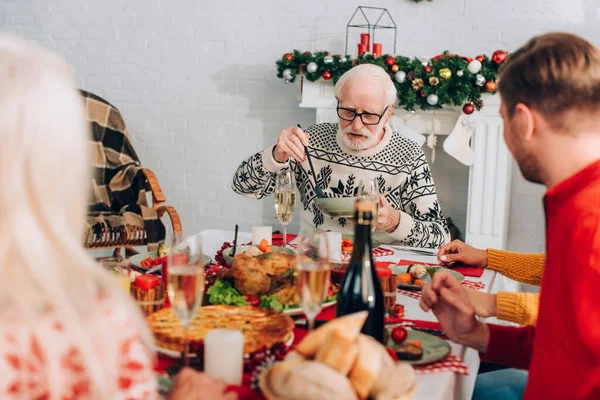 Foco seletivo do homem idoso servindo comida, sentado com a família perto da lareira — Fotografia de Stock