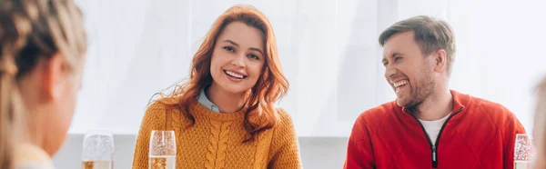 Imagen panorámica de la pelirroja sonriendo y sentada cerca del hombre riendo en casa - foto de stock