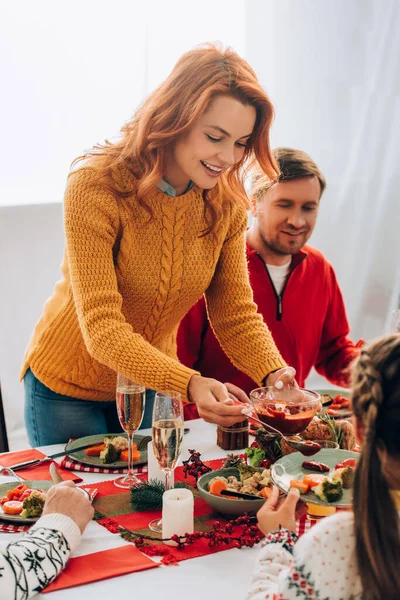 El foco selectivo de la madre feliz sirviendo salsa en el plato en la mesa festiva - foto de stock