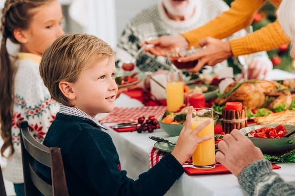 Selektiver Fokus des kleinen Jungen, der ein Glas Saft in der Hand hält und am festlichen Tisch sitzt — Stockfoto