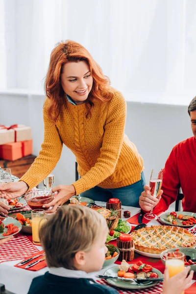 Selective focus of redhead woman serving sauce at festive table near family — Stock Photo