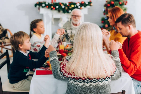 Selective focus of senior woman holding hands with family while sitting at table — Stock Photo