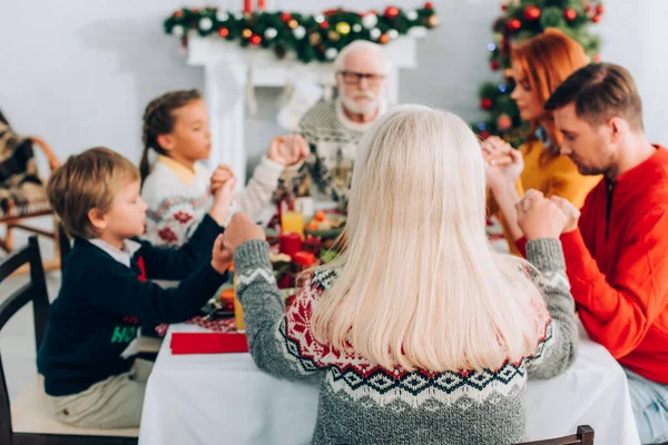 Concentration sélective de la femme âgée tenant la main avec la famille tout en étant assis à la table — Photo de stock