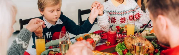 Colpo panoramico di ragazzo che si tiene per mano con la famiglia, seduto al tavolo festivo — Foto stock