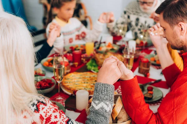 Selective focus of woman and man holding hands near family, sitting at table — Stock Photo