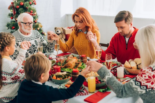 Familia cogida de la mano mientras se sienta en la mesa festiva con cena de acción de gracias - foto de stock