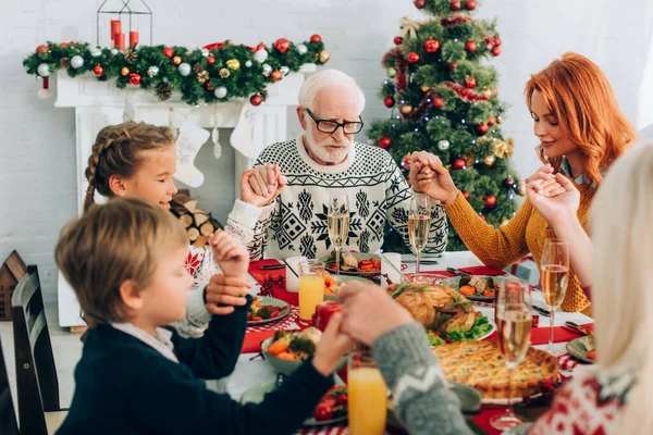 Selective focus of grandfather holding hands with family, sitting near fireplace — Stock Photo