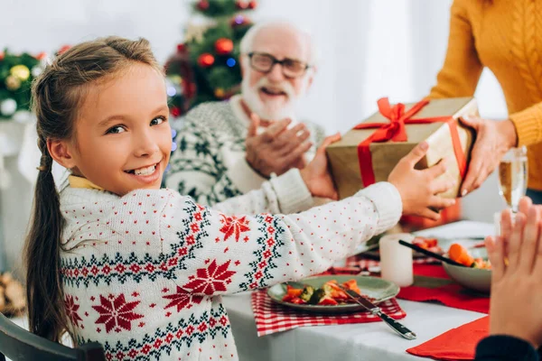 Foyer sélectif de fille souriante avec cadeau de la mère, assis à la table festive — Photo de stock