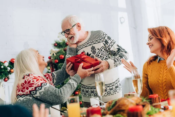 Smiling grandfather greeting wife with present near family applauding at home — Stock Photo