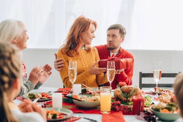 Selective focus of husband embracing wife with present near relatives at home — Stock Photo