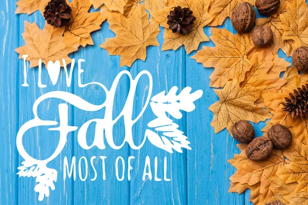 Top view of autumnal foliage with nuts and cones near i love fall most of all lettering on blue wooden background — стоковое фото