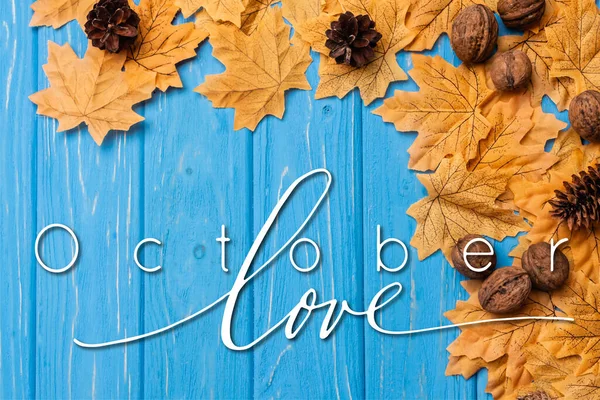 Blick von oben auf herbstliches Laub mit Nüssen und Zapfen in der Nähe von Oktober Love Schriftzug auf blauem Holzgrund — Stockfoto