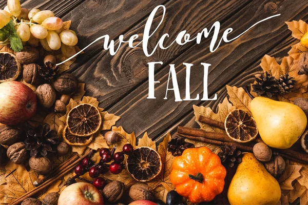 Top view of autumnal harvest and foliage near welcome fall lettering on brown wooden background — Stock Photo