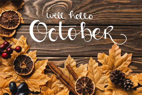 Top view of autumnal decoration and foliage near well hello october lettering on wooden background — Stock Photo