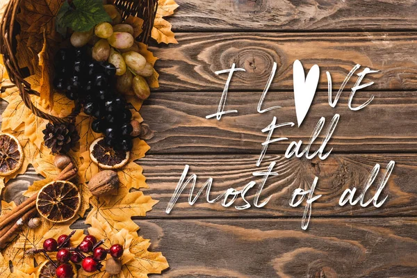 Top view of autumnal harvest scattered from basket on foliage near i love fall most of all lettering on wooden background — Stock Photo
