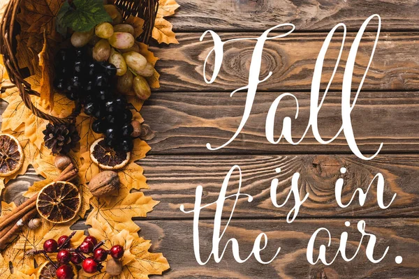 Top view of autumnal harvest scattered from basket on foliage near fall is in the air lettering on wooden background — Stock Photo